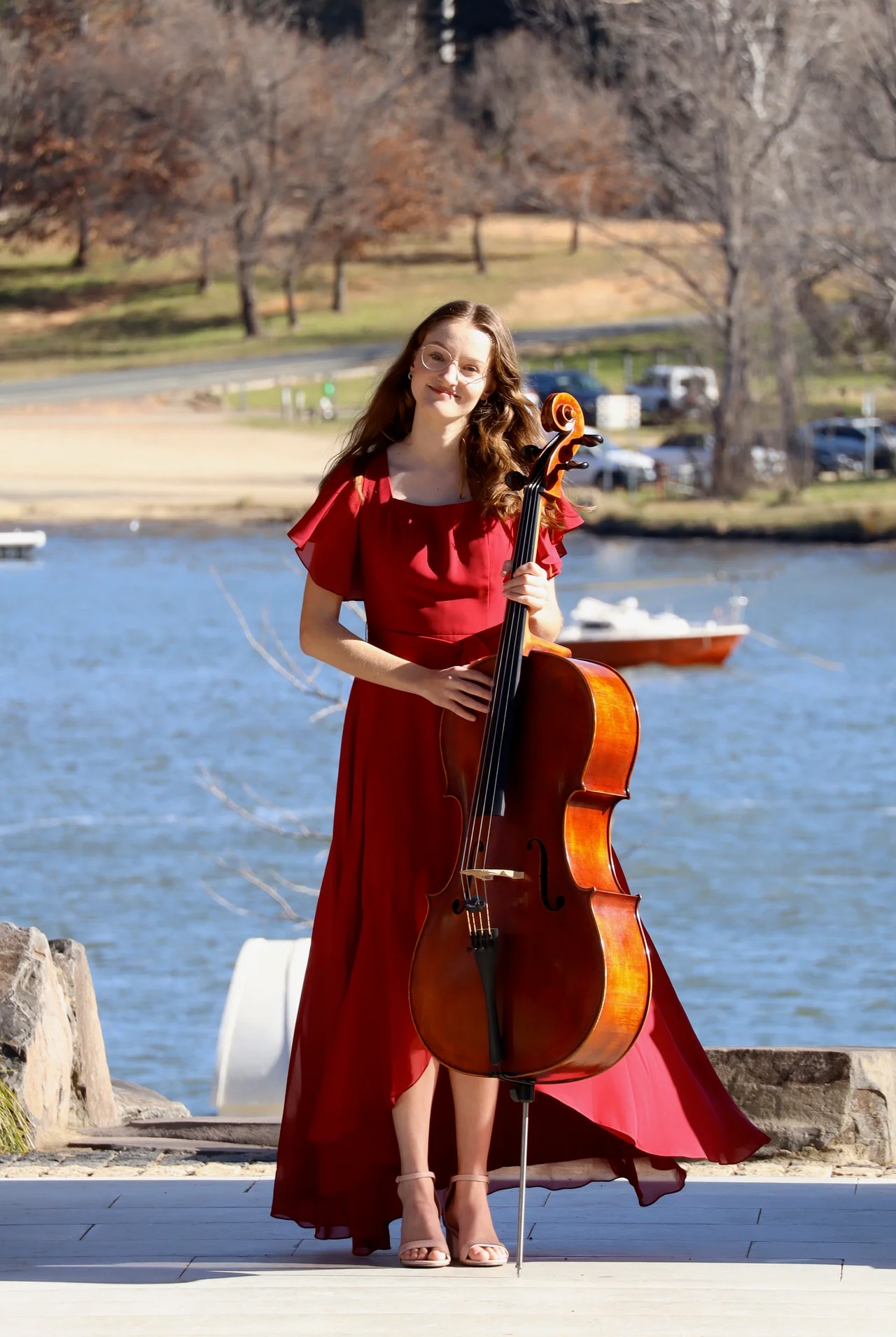 Joanna holding her cello beside the lake