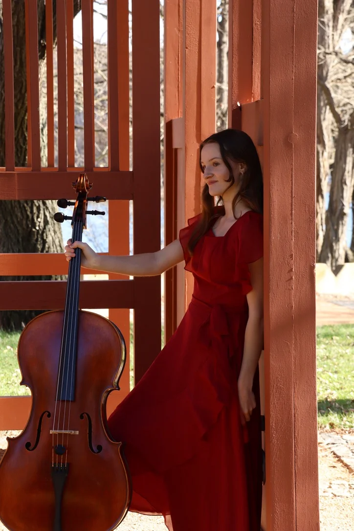 Joanna with her cello beside a red timber pavilion